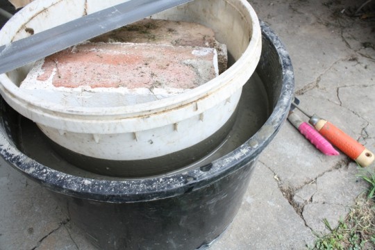 Cement leveled, bricks weighing down the mold, tape keeping it level up and down.