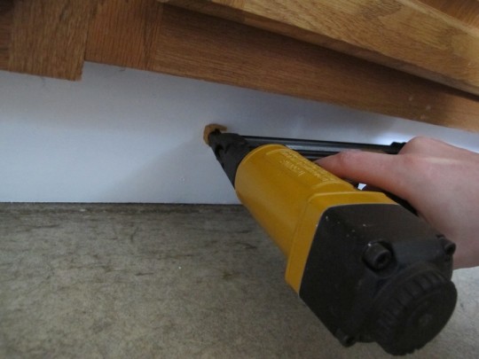 Reattaching painted plywood beneath the cabinets.