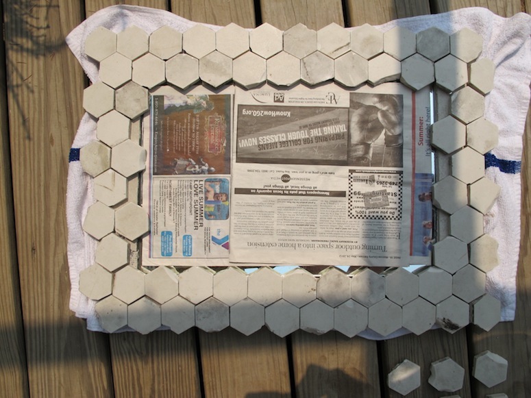 Vintage marble hex tiles positioned around the edge of a mirror protected by newspaper.