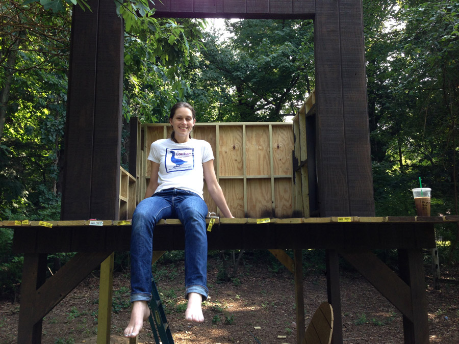 Woman sitting on the ledge of a backyard treehouse before installing safety railings.