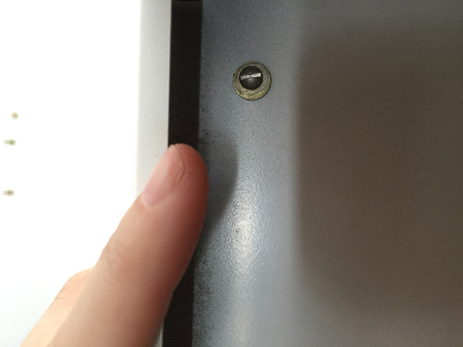 A finger points at a bolt used to attach two cabinets together.