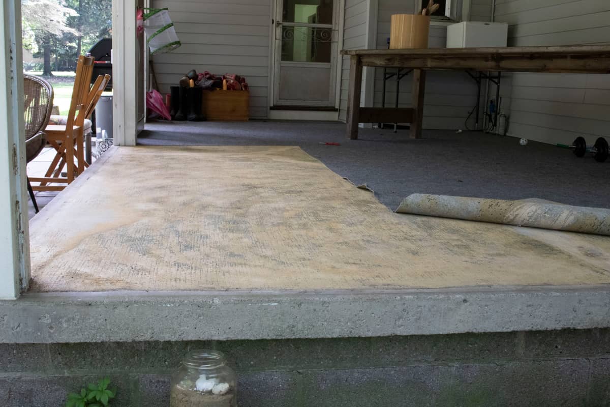 Removing an old outdoor carpet on a covered patio and revealing the underlying adhesives.