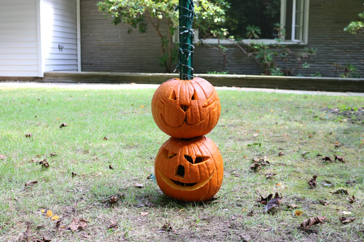 Two carved pumpkins threaded on a post to form a totem pole.